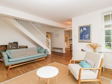 A living room with a blue sofa a white armchair a round white table a rug wooden flooring and a staircase at Tor Cottage in Colwall Herefordshire