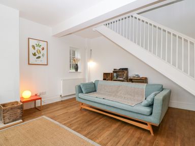 A living room with a blue sofa under white stairs and wooden crate shelves at Tor Cottage in Colwall Herefordshire