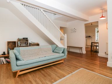 A living room with a blue sofa under a staircase and wooden floor at Tor Cottage in Colwall Herefordshire