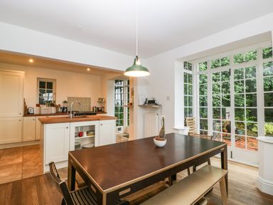A kitchen and dining area with a wooden dining table and bench next to large windows overlooking a garden at Tor Cottage in Colwall Herefordshire