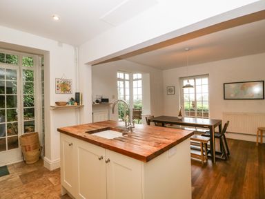 A kitchen island with a wooden countertop and sink next to a dining table and chairs in a room with large windows at Tor Cottage in Colwall Herefordshire