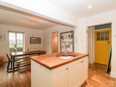 A kitchen with a wooden island countertop and a dining table with chairs and a bench at Tor Cottage in Colwall Herefordshire