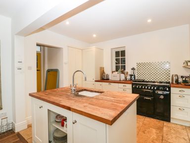 A kitchen with a wooden island counter and a black stove at Tor Cottage in Colwall Herefordshire