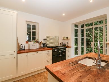 A kitchen with wooden countertops a sink a black stove white cabinets and large windows at Tor Cottage in Colwall Herefordshire