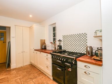 A kitchen with cream cabinets wooden countertops a black stove and a yellow door at Tor Cottage in Colwall Herefordshire