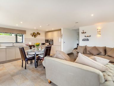 An open plan kitchen and living area with a dining table set for four and two sofas at Secret Kingdom Cottage in Warkworth