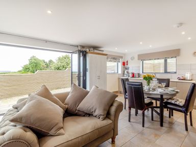 An open plan kitchen and dining area with a sofa and round dining table set with dishes at Secret Kingdom Cottage in Warkworth
