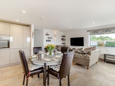 A kitchen and living room area with a dining table set for four and sofas near a wall-mounted TV at Secret Kingdom Cottage in Warkworth