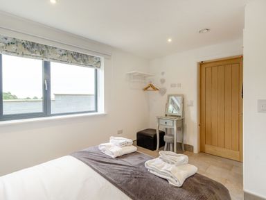 A bedroom with a bed towels window dressing table stool and wooden door at Secret Kingdom Cottage in Warkworth
