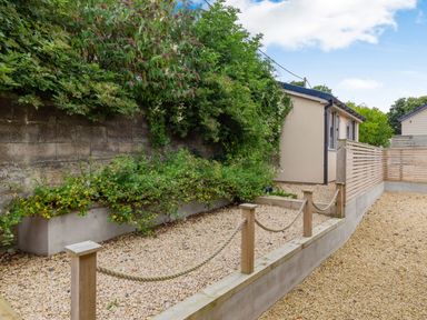 A garden area with gravel paths bordered by wooden posts connected with rope and plants along a stone wall at Secret Kingdom Cottage in Warkworth