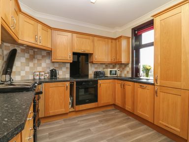 A kitchen with wooden cabinets and black countertops a kettle toaster and microwave on the counters and a bouquet of flowers by the window at Silver Crooks in Trewyn Nr Holsworthy