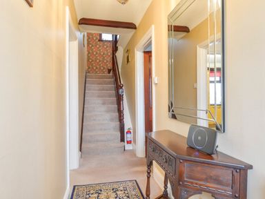 A hallway with a carpeted staircase a wooden table with a black speaker and a large mirror on the wall at Silver Crooks in Trewyn Nr Holsworthy