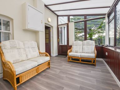 A conservatory with two wicker sofas with cushions and large windows at Silver Crooks in Trewyn Nr Holsworthy