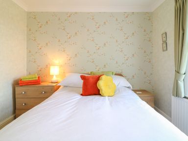 A bedroom with a bed white bedding and colorful cushions a lamp on a wooden nightstand at Silver Crooks in Trewyn Nr Holsworthy