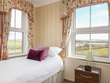 A bedroom with a single bed purple pillows floral curtains and a bedside table with a lamp and clock at Silver Crooks in Trewyn Nr Holsworthy