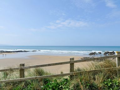 A sandy beach with a wooden fence in the foreground and ocean waves at Silver Crooks in Trewyn Nr Holsworthy