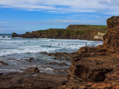 A rocky coastline with waves and people surfing in the water at Silver Crooks in Trewyn Nr Holsworthy