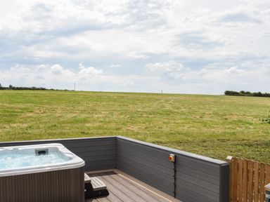 A hot tub on a wooden deck overlooking a grass field at Silver Crooks in Trewyn Nr Holsworthy