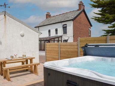 An outdoor patio with a hot tub and wooden picnic table near a white building and a brick house at Silver Crooks in Trewyn Nr Holsworthy