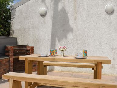 An outdoor patio with a wooden picnic table set with plates cups and flowers near a brick barbecue at Silver Crooks Trewyn Nr Holsworthy
