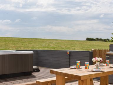 An outdoor deck with a wooden table set for four and a hot tub overlooking a grassy field at Silver Crooks in Trewyn Nr Holsworthy