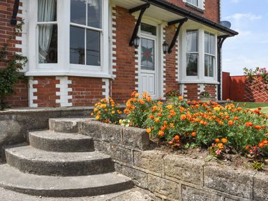 A concrete curved staircase leading to a white door with stained glass and orange flowers in the garden of a red brick house at Silver Crooks in Trewyn Nr Holsworthy