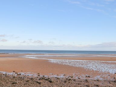 A beach with wet sand and rocks near the shore under a clear sky at 4 Parc Delfryn in Brynteg near Benllech