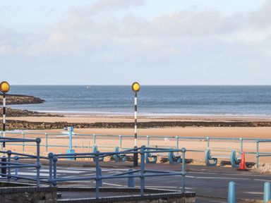 A beach with sandy shore and sea beyond viewed from across a road with railings and yellow road lights at 4 Parc Delfryn in Brynteg near Benllech