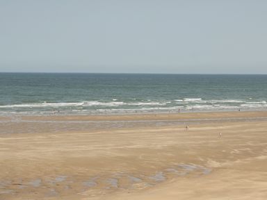 A wide sandy beach with small groups of people near the shoreline and a calm sea at 4 Parc Delfryn in Brynteg near Benllech