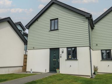 Front exterior of a modern two-story house with green upper cladding white lower walls a green door and windows at 4 Parc Delfryn in Brynteg near Benllech