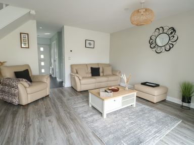 A living room with beige sofas a wooden coffee table a decorative wall mirror and a gray rug at 4 Parc Delfryn Brynteg near Benllech