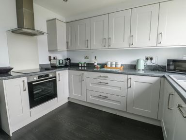 A kitchen with white cabinets black countertops an oven a toaster a kettle and a microwave at 4 Parc Delfryn Brynteg near Benllech