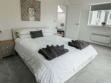 A bedroom with a bed white bedding dark towels bedside tables lamps and a Buddha painting at 4 Parc Delfryn in Brynteg near Benllech
