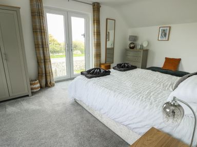 A bedroom with a bed a dresser a wardrobe full length mirror and double doors with yellow curtains at 4 Parc Delfryn Brynteg near Benllech