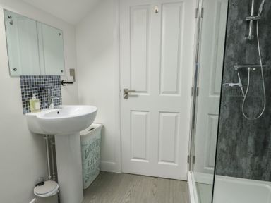 A bathroom with a sink and mirror near a white door and a glass-enclosed shower at 4 Parc Delfryn Brynteg near Benllech