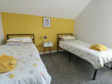 A bedroom with two single beds and a bedside table against a yellow and white wall at 4 Parc Delfryn in Brynteg near Benllech