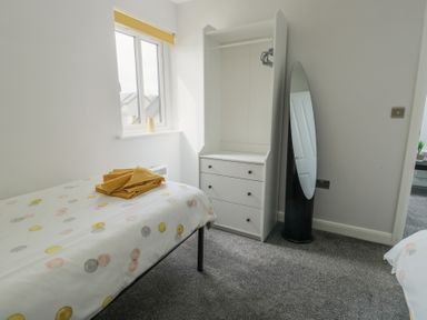 A bedroom with a single bed with polka dot bedding folded towels a white dresser and a full length mirror at 4 Parc Delfryn in Brynteg near Benllech
