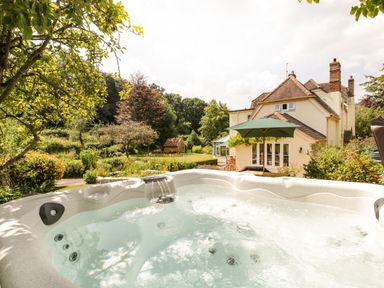 An outdoor hot tub with water jets in a garden with trees and a house in the background at Valley House in Devizes