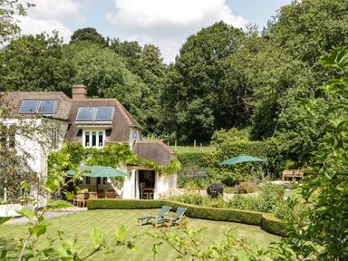 A garden with lounge chairs umbrellas and hedges next to a house with solar panels at Valley House in Devizes