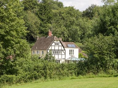 A white house with black timber framing surrounded by trees and greenery at Valley House in Devizes