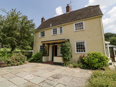 Exterior of a two-story house with a tiled roof, front porch, paved driveway, and bushes at Valley House in Devizes