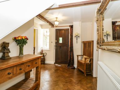 An entryway with a wooden door a wooden bench with a pillow a wooden table with drawers flowers in a vase and a bust on top and a large ornate wall mirror at Valley House in Devizes