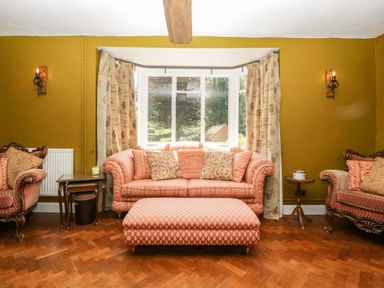 A sitting room with patterned sofas and ottoman in front of a window with curtains at Valley House in Devizes