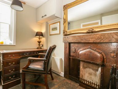 A study room with a wooden desk leather chair brass lamp and a fireplace with a large ornate mirror at Valley House in Devizes