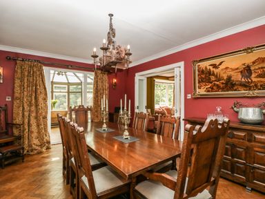 A dining room with wooden table and chairs red walls and a painting at Valley House in Devizes