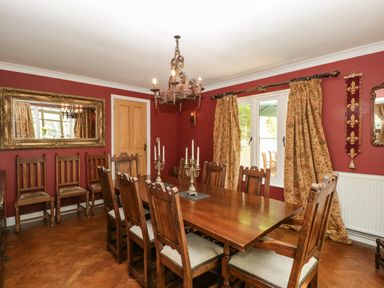 A dining room with a wooden table and chairs red walls and patterned curtains at Valley House in Devizes