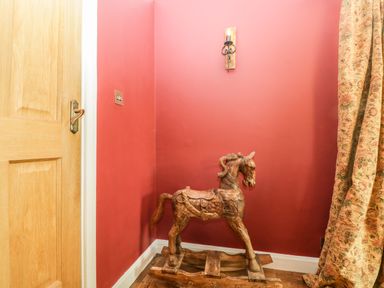 A wooden rocking horse in the corner of a room with red walls a wooden door and patterned curtains at Valley House in Devizes