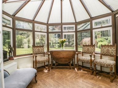 A conservatory with patterned chairs a wooden drop leaf table with flowers and a blue chaise lounge at Valley House in Devizes