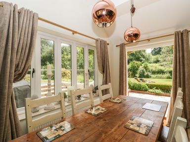 A dining room with a wooden table and white chairs next to windows and a door opening to a garden at Valley House in Devizes