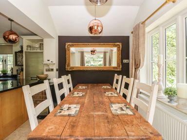 A dining room with a wooden table and white chairs next to windows with curtains and a large decorative mirror on a wall at Valley House in Devizes
